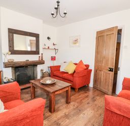 A living room with red sofas wooden coffee table and a fireplace at Carrstone Cottage in Heacham