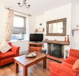 A living room with two red armchairs a wooden coffee table a fireplace and a TV at Carrstone Cottage in Heacham