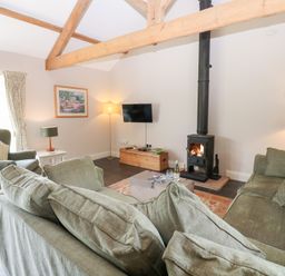 A living room with a sofa, armchair, and wood stove at Shepherds Burn Cottage in Bellingham
