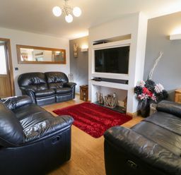 A living room with black leather sofas a mounted television a red rug and a vase with flowers at 6 Stad Yr Ysgol in Manod near Blaenau Ffestiniog