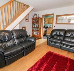 A living room with two black leather sofas a wooden bookshelf and a red rug at 6 Stad Yr Ysgol in Manod near Blaenau Ffestiniog
