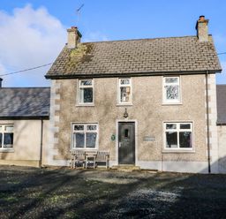 The front exterior of a two story stone cottage with a bench and a door at Rosies Cottage in Bushmills County Antrim