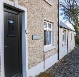 The exterior of Rosies Cottage with a black door a window a green self catering sign and a gravel path at Rosies Cottage in Bushmills County Antrim