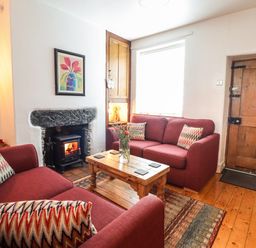 A living room with two red sofas a wooden coffee table a fireplace and a wooden door at Siskin in Dinas Mawddwy near Dolgellau