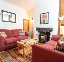 A living room with two red sofas a wooden coffee table and a fireplace at Siskin in Dinas Mawddwy near Dolgellau