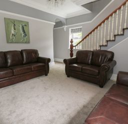 A sitting room with three brown leather sofas a painting of two hares on the wall and a staircase at Dumbuie in Haltwhistle