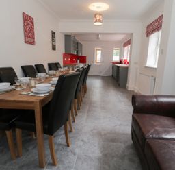 A dining area with a wooden table set with dishes and black chairs next to a kitchen with grey cabinets and red backsplash at Dumbuie in Haltwhistle