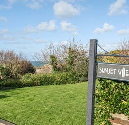 A sign for Sunset View near grass and trees in Porth