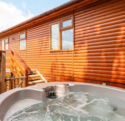 A hot tub with bubbling water next to wooden steps and a log cabin exterior at Callow Lodge 22 in Beaconsfield Holiday Park