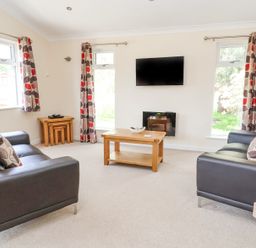 A living room with two black sofas a wooden coffee table a wall-mounted TV and patterned curtains at Callow Lodge 22 Beaconsfield Holiday Park