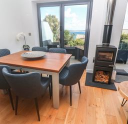 A dining area with a wooden table surrounded by six blue chairs near a stove and glass doors opening to an outdoor seating area with a view at Seafield in Carbis Bay near St Ives
