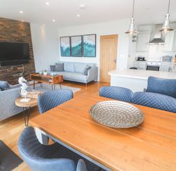 An open plan living room and kitchen with blue chairs a wooden dining table light grey sofas and a wall mounted television at Seafield in Carbis Bay near St Ives