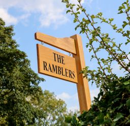 A wooden sign reading The Ramblers hanging outdoors near green foliage and trees at The Ramblers' Annex in Mattishall