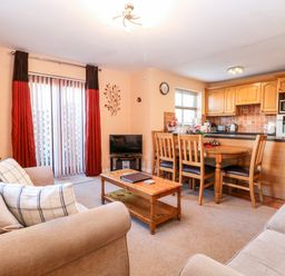 A living room with a beige sofa coffee table dining table and kitchen area at The Ramblers Annex in Mattishall