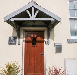 A wooden door with a small window under a gray porch roof with a sign reading The Old Chapel and a mailbox on the wall at Old Chapel in Cloughton