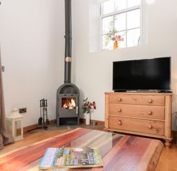A living room with a wood stove a TV on a wooden chest of drawers and a coffee table at Old Chapel in Cloughton