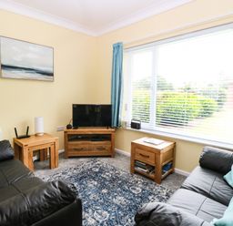 A living room with two black sofas a blue rug wooden tables a television and a large window with blue curtains at 20 Siesta Mar in Mundesley