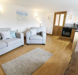 A living room with grey sofa and armchair near a kitchen with wooden cabinets at The Annex @ Garden House in Prudhoe near Newcastle