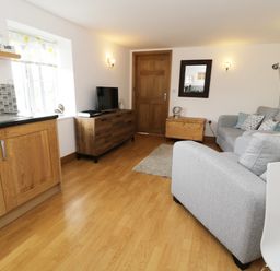 A living room with a gray sofa a wooden cabinet a wooden door and a kitchen area at The Annex @ Garden House Prudhoe near Newcastle