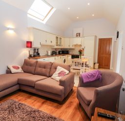 An open plan living room and kitchen with a sofa armchair dining table and wooden floor at Laharn Cottage in Killorglin County Kerry