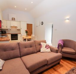 An open living room and kitchen with a brown sofa, armchair, round dining table, and kitchen cabinets at Laharn Cottage in Killorglin County Kerry