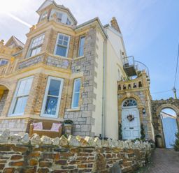 A stone and brick house with white windows a white door with a wreath and a stone wall at Spiral View in Perranporth