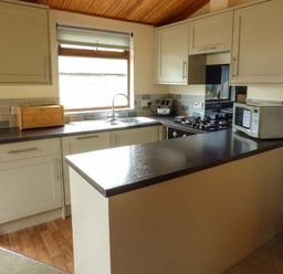 A kitchen with cabinets a countertop a gas stove a microwave a sink and a wooden breadbox at South Lodge in Kendal