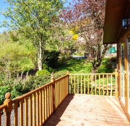 A wooden deck with a railing attached to a house overlooking a garden of trees and bushes at North Lodge in Kendal