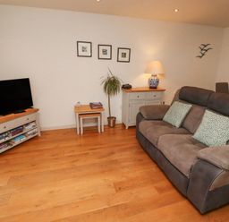 A living room with a grey sofa two cushions a television on a wooden stand two small tables a lamp and framed pictures on the wall at 6 Mill Wharf in Berwick-upon-Tweed