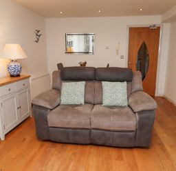 A living room with a gray sofa two cushions wooden floor mirror sideboard and a door at 6 Mill Wharf in Berwick-upon-Tweed