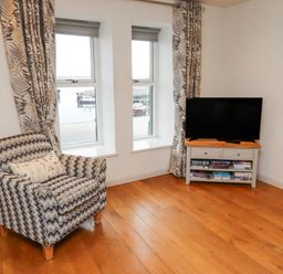 A living room with an armchair by two windows and a TV on a cabinet with books at 6 Mill Wharf in Berwick-upon-Tweed