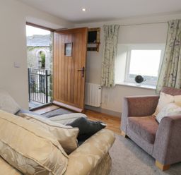 A seating area with two armchairs a small window with curtains and an open wooden door at The Granary Loft in Bardsea