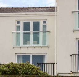A building facade with glass balconies and windows above bushes at Harbour View in Cemaes Bay