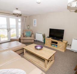 A living room with leather sofas a wooden coffee table a television and glass doors overlooking the sea at Harbour View in Cemaes Bay