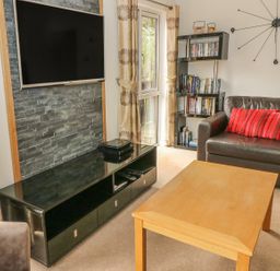 A living room with a wall mounted television glass cabinet wooden coffee table leather sofa with red cushions and a bookshelf at Coniston Number 9 in White Cross Bay