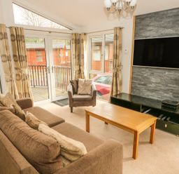 A living room with sofa armchair coffee table television and large windows at Coniston Number 9 in White Cross Bay