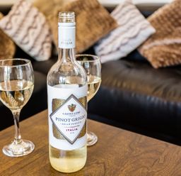 A bottle of white wine and two glasses on a wooden table in front of a couch with cushions at Tus Nua Cottage in Carhampton