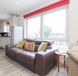 A living room with a brown leather sofa with cushions next to a window and kitchen cabinets visible in the background at Jakanori in Staveley