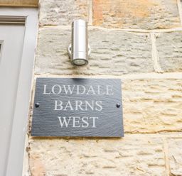 A stone wall with a gray plaque reading lowdale barns west and a silver outdoor light above it at Lowdale Barns West in Sleights