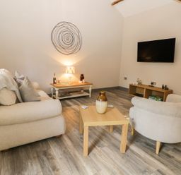 A living room with two beige sofas a wooden coffee table with a vase a wall-mounted TV and a small side table with a lamp at Lowdale Barns West in Sleights