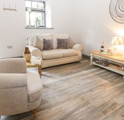 A living room with a beige sofa and armchair wooden coffee table lamp and decorative items at Lowdale Barns West in Sleights