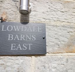A stone wall with a rectangular plaque reading Lowdale Barns East and a metal light fixture above at Lowdale Barns East in Sleights