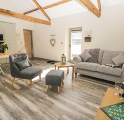 An open living area with a gray sofa, gray armchair, small table with a lantern, dining table with chairs and kitchen appliances at Lowdale Barns East in Sleights