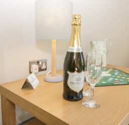 A wooden table with a bottle of prosecco two glasses a table lamp a metal jug and a scrabble game at Lowdale Barns East in Sleights