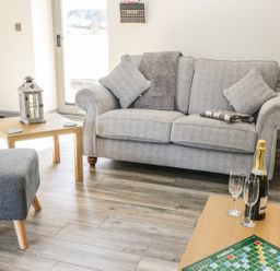 A living room with a gray sofa pillows blankets a wooden coffee table lantern ottoman champagne bottle glasses and a scrabble game at Lowdale Barns East in Sleights