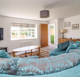 A living room with a curved teal patterned sofa a wooden coffee table a wall mounted TV and a wooden sideboard at 8 Pottergate Mews in Helmsley