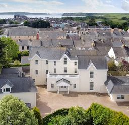 An aerial view of a residential area with white buildings trees and a body of water in the background at Harbour Beach at The Hideaway in Tenby