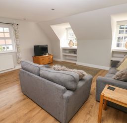 A living room with two grey sofas a wooden TV stand with a television and wooden side table with a lamp at North Beach at The Hideaway in Tenby