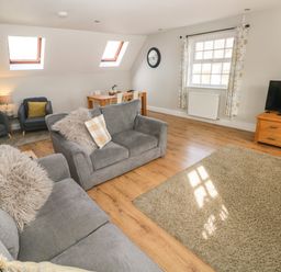 A living room with gray sofas a wooden dining table chairs a television on a wooden stand and windows at North Beach at The Hideaway in Tenby