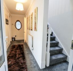 A hallway with carpeted stairs a brown rug a wall mirror and framed pictures at 11 Glyn Garth Mews in Llandegfan near Beaumaris